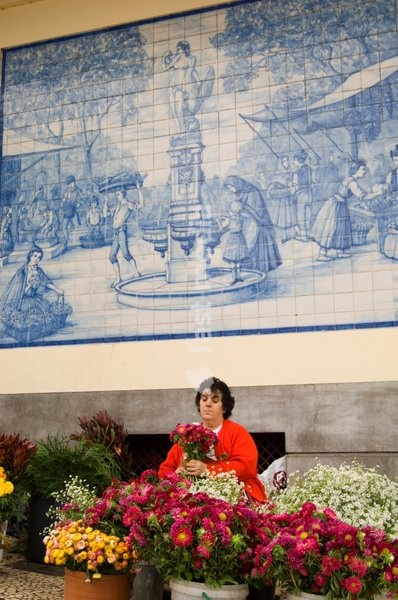 A woman selling flowers outside the main market, in front of a mural made from old Portuguese blue and white tiles, Funchal, Madeira, Portugal, Europe