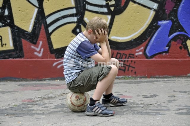Disappointed and lonely boy with his football in front of a graffiti wall, kickabout area in Cologne, North Rhine-Westphalia, Germany, Europe
