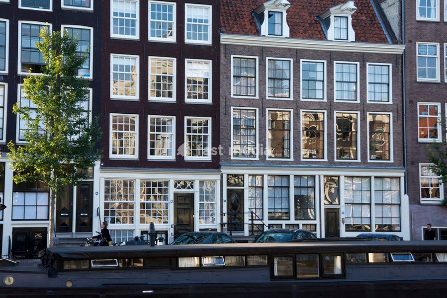 House row at one of the canals in the Amsterdam centre. In the foreground, a houseboat. Photography