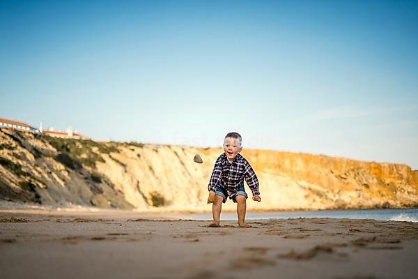 Small boy throwing stones on the beach by the sunset, Portugal