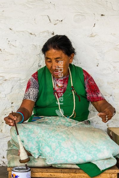 An older Tibetan refugee woman spins wool into yarn by hand for making rugs in a refugee settlement in Pokhara, Nepal