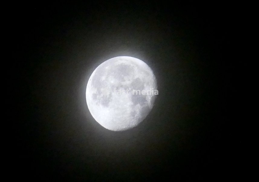 A thin veil of mist surrounds the waning gibbous moon visible at 90.9% in the early mornings sky