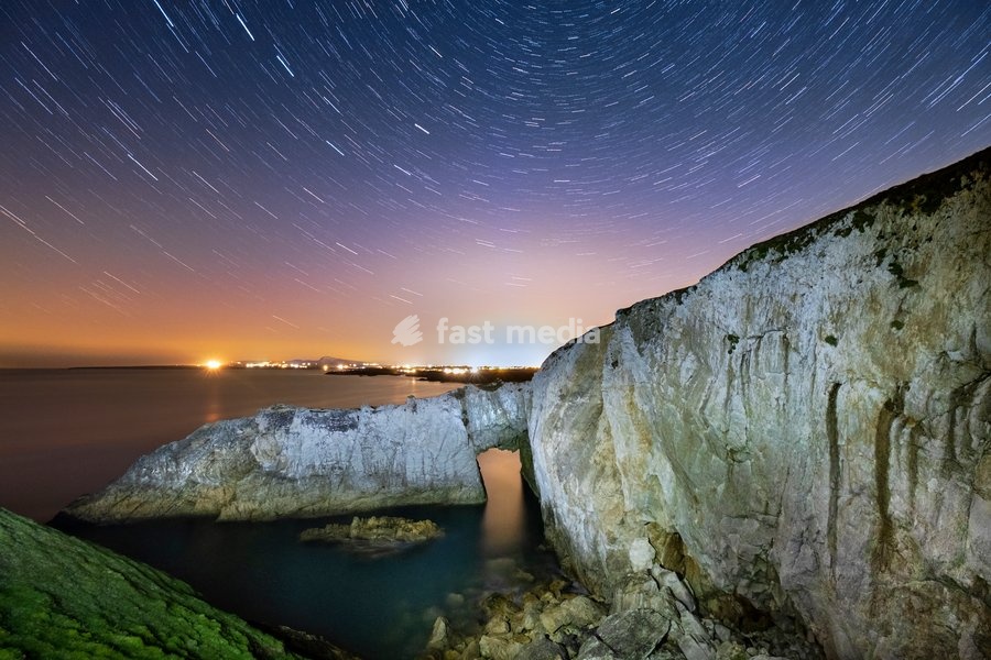 Star trails and night sky over Bwa Gwyn or the White Arch, near Rhoscolyn, Anglesey, North Wales, United Kingdom, Europe