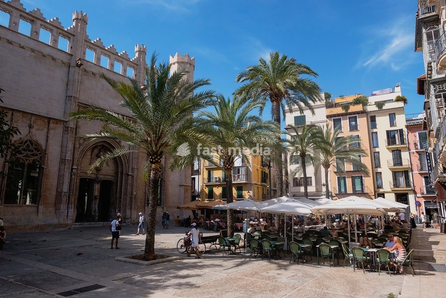 Spain, Balearic Islands, Majorca, Palma de Mallorca, Old Town. Placa de La Llotja. People at restaurant table under umbrellas in the old market square