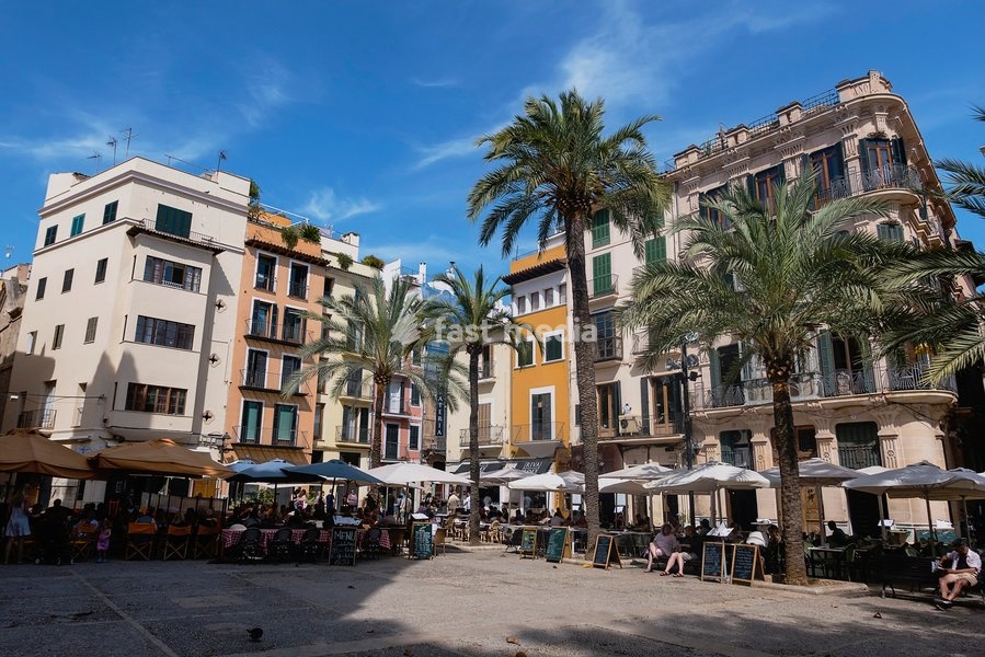 Spain, Balearic Islands, Majorca, Palma de Mallorca, Old Town. Placa de La Llotja. People at restaurant table under umbrellas in the old market square
