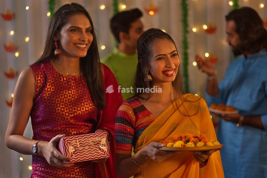 Smiling women standing with gift and flowers during Diwali celebration