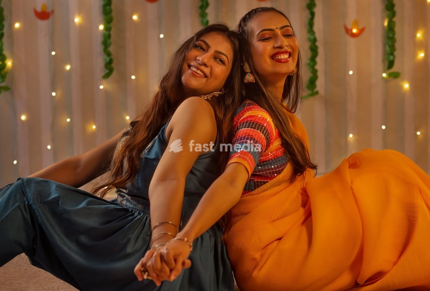 Portrait two cheerful young women sitting back-to-back during Diwali celebration