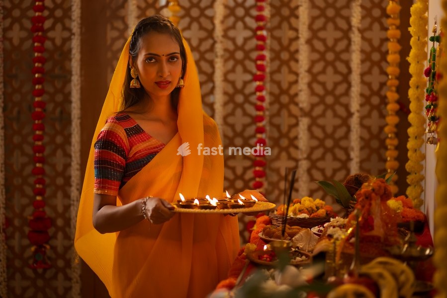 Portrait of Indian woman holding a plate of diyas and worshiping God on Diwali