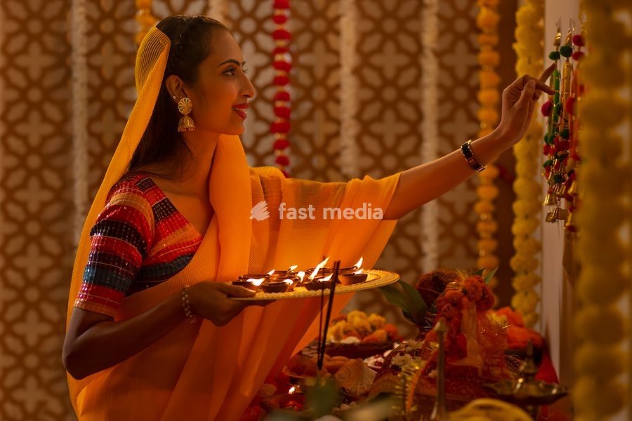Portrait of Indian woman holding a plate of diyas and worshiping God on Diwali