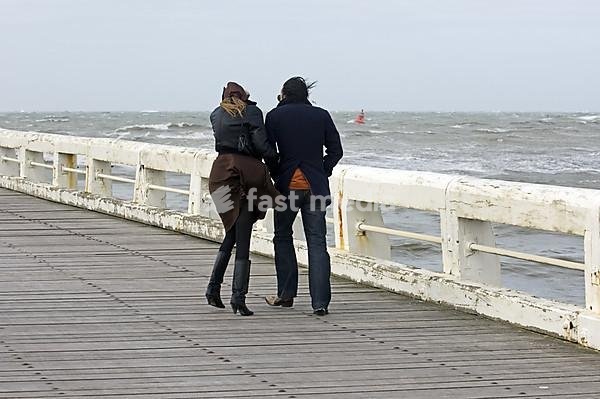 Koppel wandelt op het Westerstaketsel tijdens storm, Oostende, België Couple walking on the western jetty during storm, Ostend, Belgium