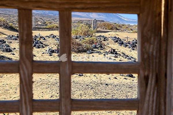 View through old gate cemetery gate cemetery door on old silted up historic cemetery from 1950s with several graves marked by stones from abandoned village village Cofete on west coast of peninsula Jandia, in the background mountains hills former volcanoes, Cofete, Jandia, Fuerteventura, Canary…