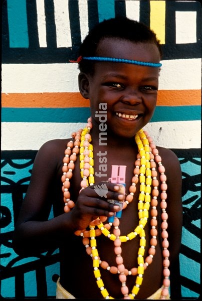 An Ndebele child, wearing beaded jewellery, poses in front of a painted wall