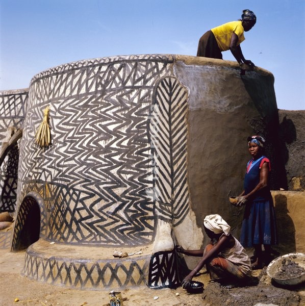 After the walls have been restored with a mixture of mud and dung, white chalk signifying purity is rubbed on to smooth the surface and add highlight. The Kassena women then use coal tar mixed with sand and boiling water to paint their traditional patterns. The tar is absorbed into the mud surface…