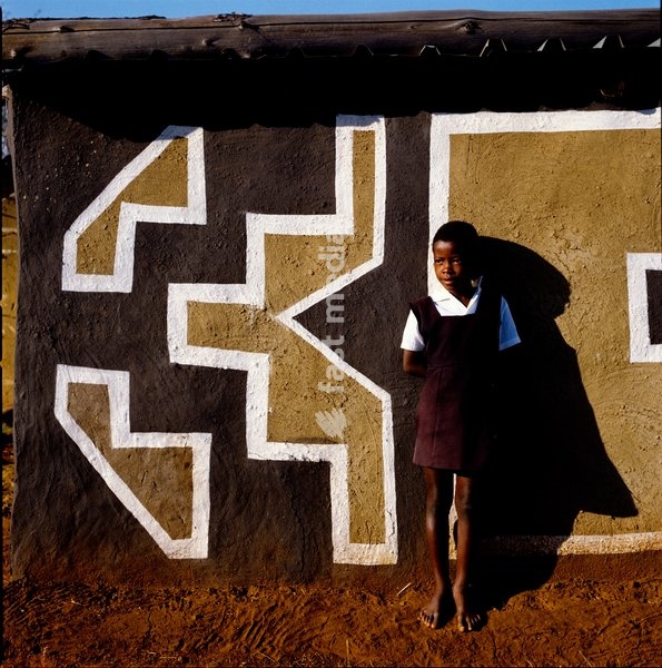 A child dressed in school uniform poses at the entrance of a building painted in geometric patterns