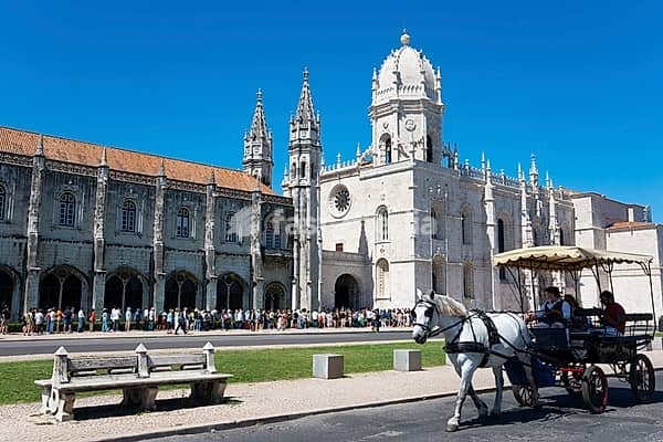Eine gotische Kathedrale unter klarem blauen Himmel mit Touristen und einer Kutsche mit Pferden im Vordergrund, Hieronymus Kloster, Mosteiro dos Jerónimos, Hieronymitenkloster, Weltkulturerbe, Klosterkirche Santa Maria, Belém, Belem, Bethlehem, Lissabon, Lisboa, Portugal, Europe