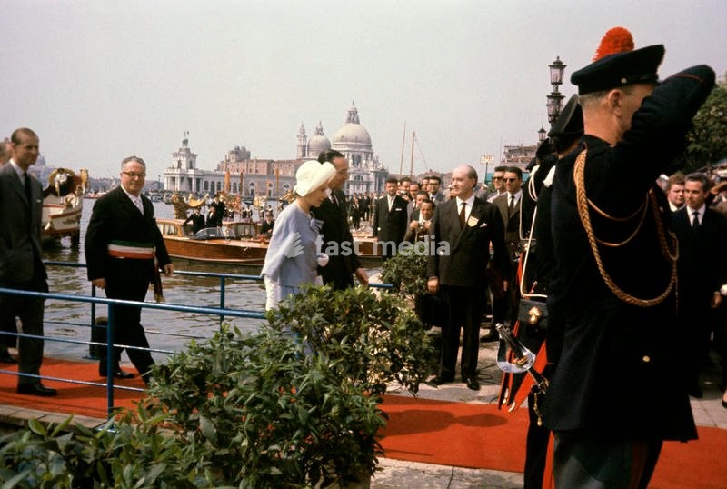 Queen Elizabeth II of the United Kingdom, visiting Venice for the first time, in the occasion of the celebrations for the national unification's centenary, crosses the red footbridge, followed by the Mayor Giovanni Favaretto Fisca and by her husband, the Prince Philip, just got off the Yacht…