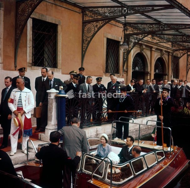 Queen Elizabeth and Prince Philip, during their visit in Italy for the celebrations of the national unification's centenary, are photographed on a motorboat, while other passengers are joining aboard; the young Queen, who had never been in Venice before, expressed her desire to visit also the side…
