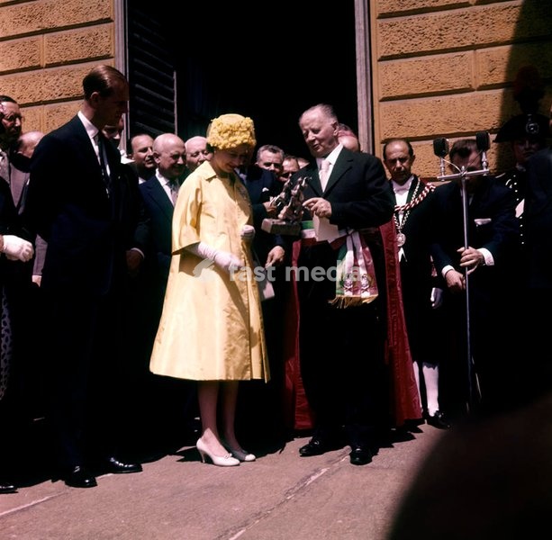 Queen Elizabeth, dressed in yellow and accompanied by her husband, the Prince Philip, Duke of Edimburgh, receives a bronze statuette by the Mayor of Castiglione Torinese, welcoming the royal couple in their visit in Italy for the centenary of the Unification; the gift commemorates the 126 british…