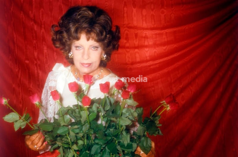 Italian actress Silvana Pampanini poses behind a beautiful bouquet of red roses looking at the camera with a red background; in the first half of the Fifties she worked with the best actors and was the symbol of Italian beauty all over the world. Italy, 1986